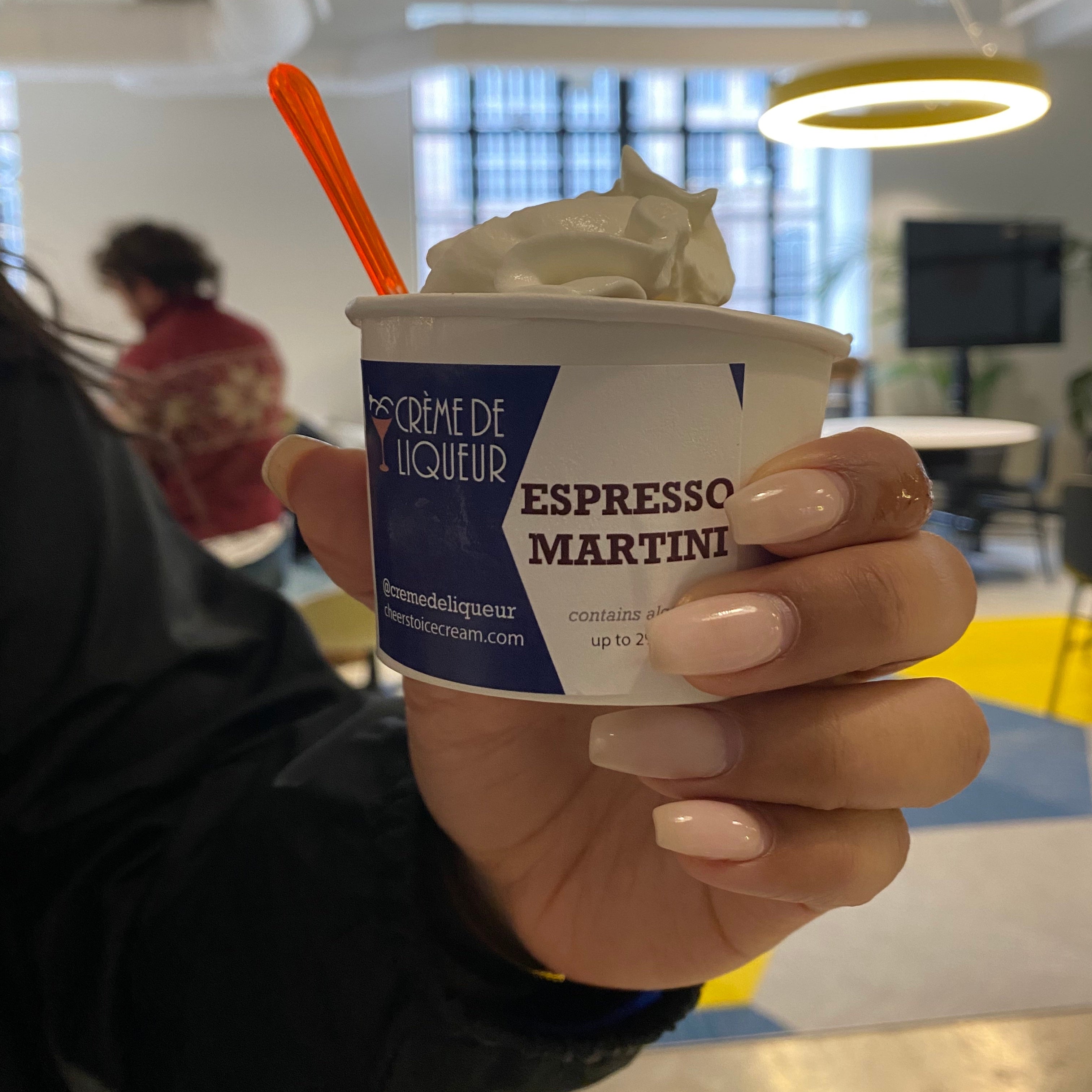 Hand holding a cup of 'Espresso Martini' dessert in a corporate office